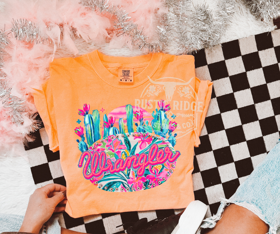 Orange t-shirt with colorful graphic and 'Wrangler' branding on a checkered surface.