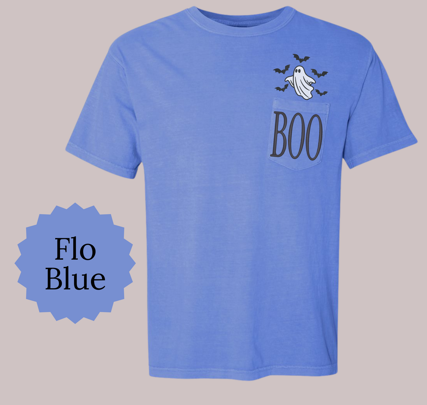 A light blue short-sleeve t-shirt with a chest pocket featuring a ghost and bats graphic above the word 'BOO' in dark gray. A blue starburst badge on the left reads 'Flo Blue'.