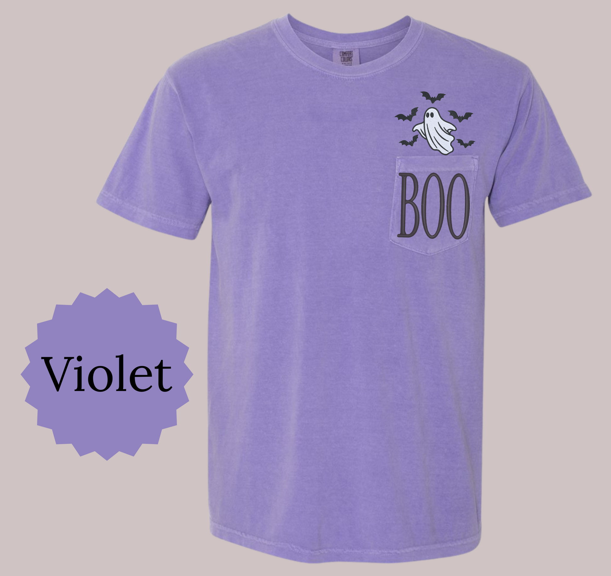 A light purple short-sleeve t-shirt with a chest pocket featuring a 'BOO' graphic with a ghost and bats, shown against a neutral beige background with a purple 'Violet' color label overlay.
