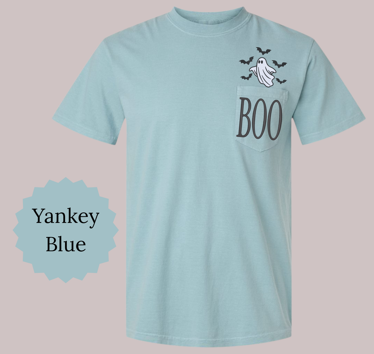 A light blue short-sleeve pocket T-shirt with a Halloween graphic on the chest pocket featuring a ghost, bats, and the word 'BOO' in dark gray. A blue starburst label on the left reads 'Yankey Blue'.