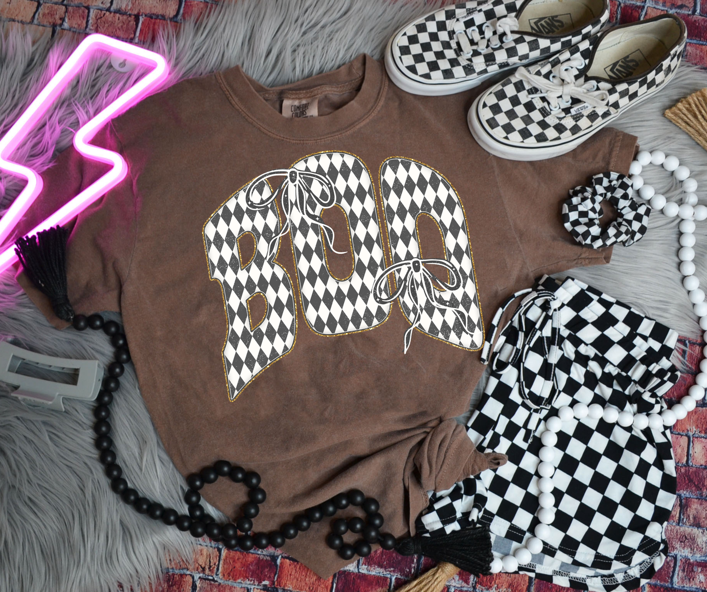 Checkered BOO Bow Graphic Tee on an Espresso Comfort Colors shirt featuring black and white harlequin lettering with bow details