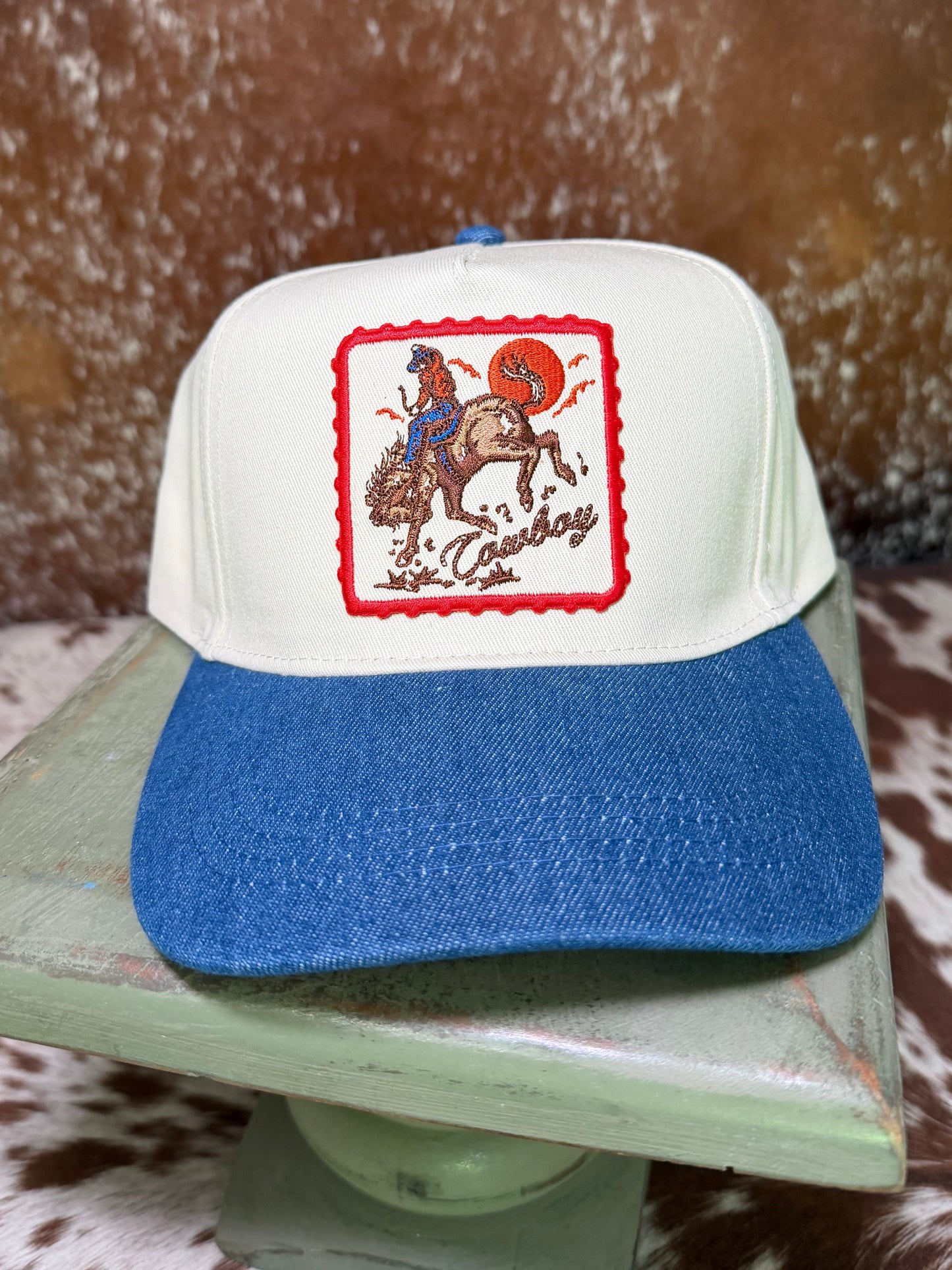 Cream and blue western trucker hat featuring an embroidered cowboy sunset rodeo patch by Rustic Ridge Customs & Co.