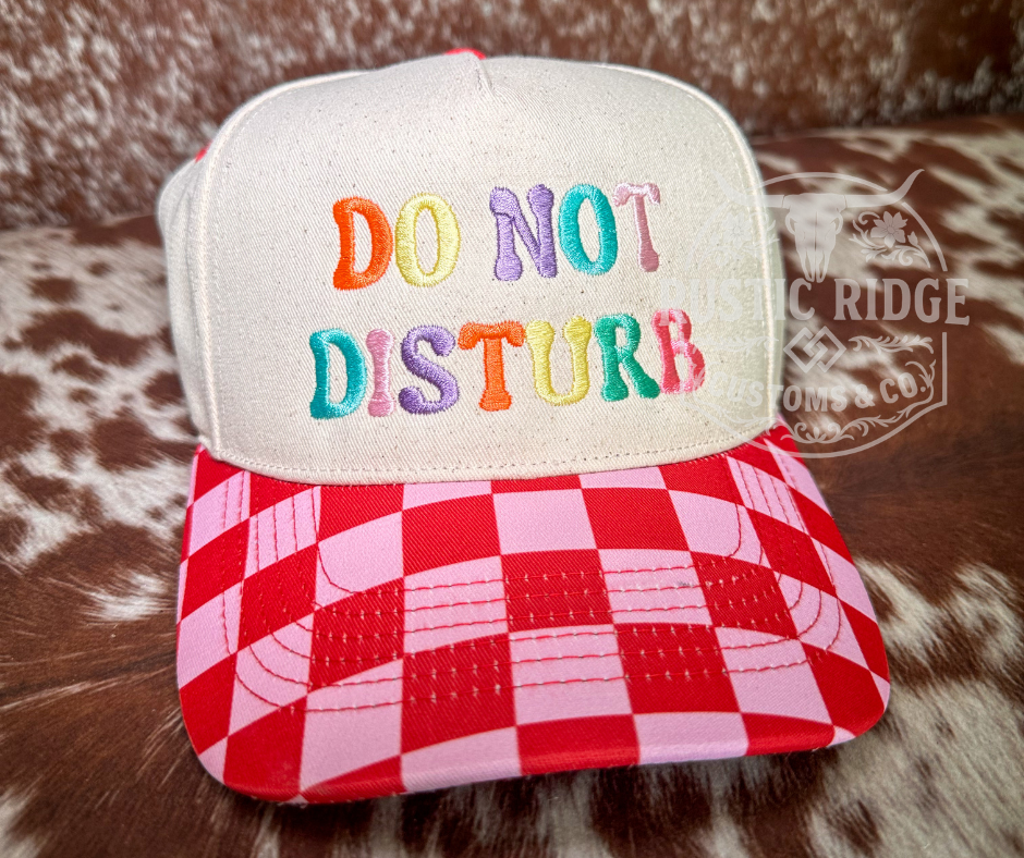 Do Not Disturb checkered trucker hat with bright colorful embroidered lettering with red and pink checkered bill by Rustic Ridge Customs & Co