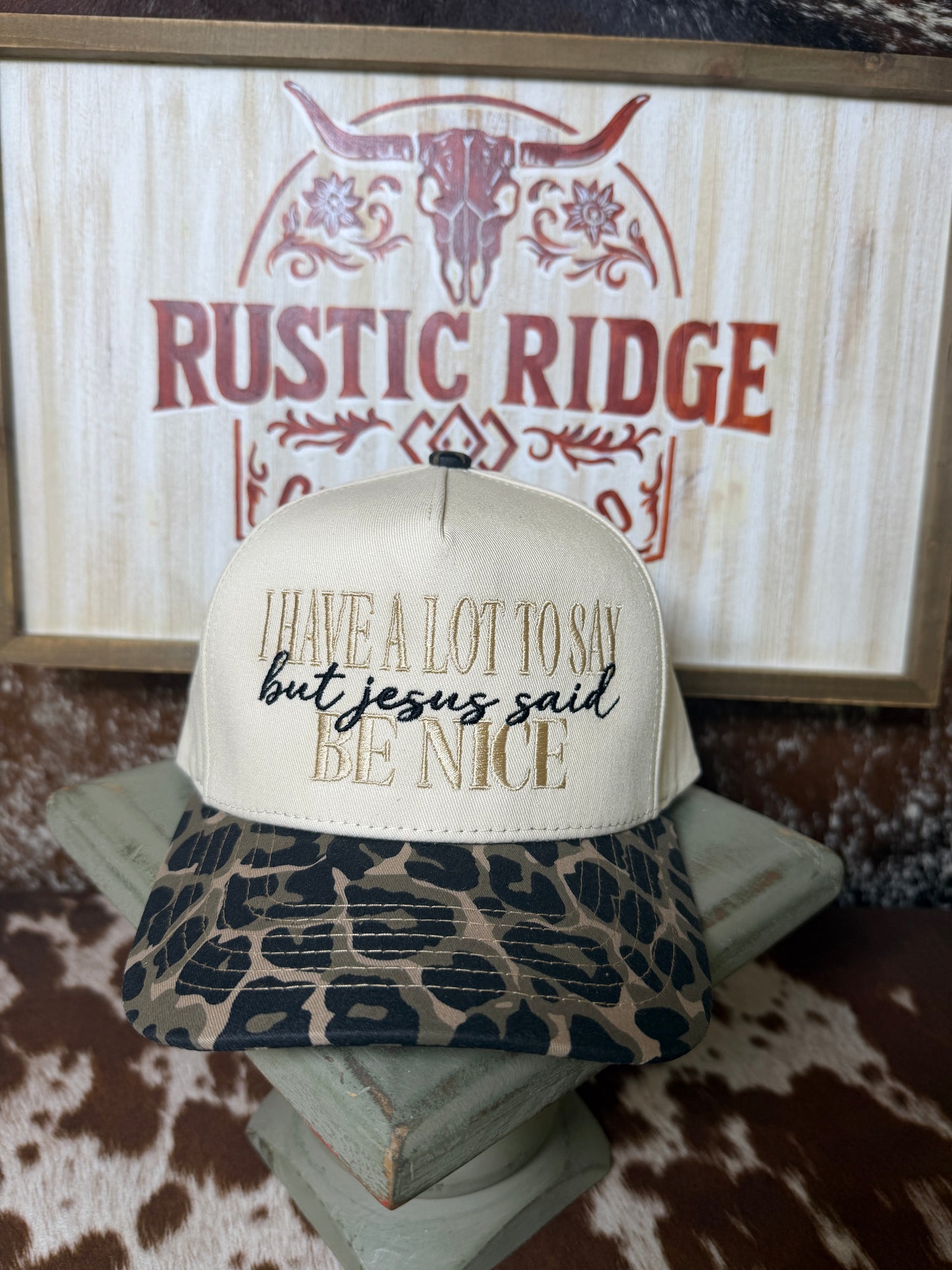 Cream and leopard print embroidered trucker hat featuring “I have a lot to say but Jesus said be nice” on the front.