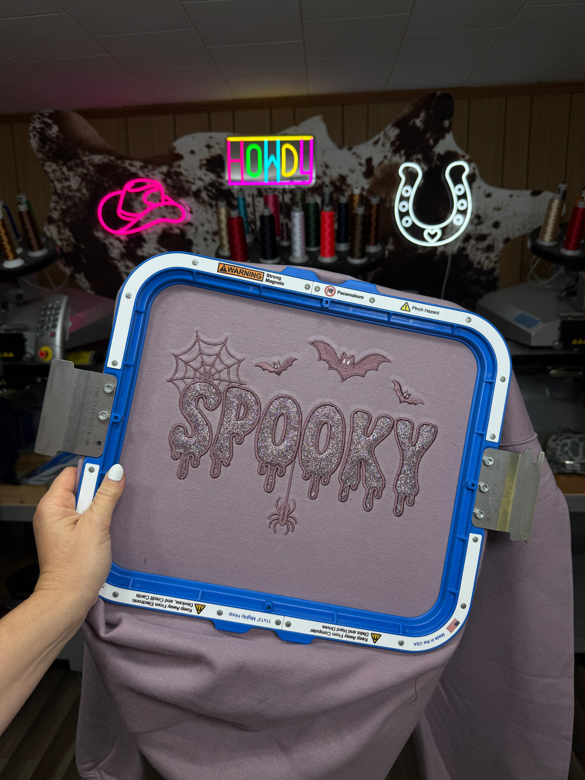 Spooky glitter embroidered sweatshirt shown in the embroidery hoop with bats, spiderweb and spider details.